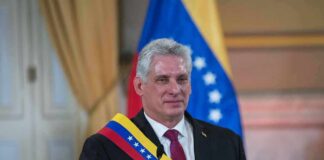 Man in suit wearing a tricolor sash seated at a podium
