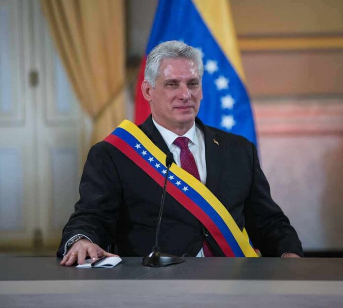Man in suit wearing a tricolor sash seated at a podium