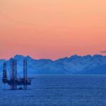An oil rig in the ocean with a backdrop of mountains during sunset