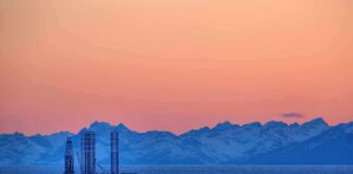 Trump Cheers — Burnham Blinks On Oil? An oil rig in the ocean with a backdrop of mountains during sunset