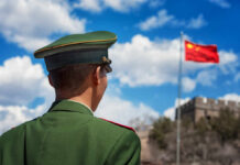A Chinese soldier in uniform standing in front of the Great Wall and the national flag