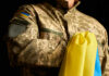 A soldier in a camouflage uniform holding a Ukrainian flag