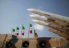 Missile launchers on a military vehicle with flags in the background