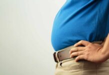 Person in a blue shirt with hands on hips, showcasing a prominent belly
