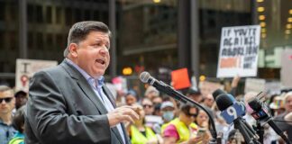 Speaker at a podium addressing a crowd with microphones and protest signs
