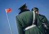 Two Chinese soldiers in military uniforms with a flag in the background