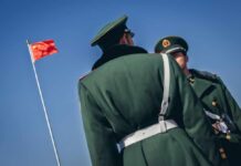 Two Chinese soldiers in military uniforms with a flag in the background