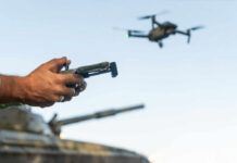 Gun-Mounted Drones: Hype Or Game-Changer? Person controlling a drone with a remote while a tank is in the background