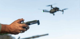 Person controlling a drone with a remote while a tank is in the background