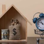 A wooden house model with money and a clock in a shopping cart