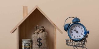 A wooden house model with money and a clock in a shopping cart