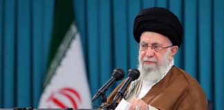 Warren Aide Praises Iran’s Hardliner A hand resting on a coffin adorned with white flowers during a funeral