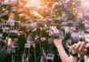 Trump DOJ Tests The Gag Line A crowd of journalists with cameras capturing an event