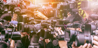 Trump DOJ Tests The Gag Line A crowd of journalists with cameras capturing an event