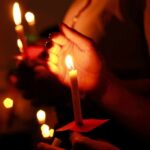 Hands holding lit candles in a dark setting