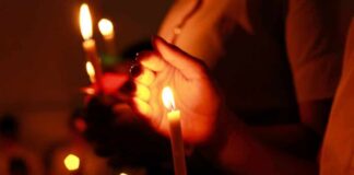 Hands holding lit candles in a dark setting