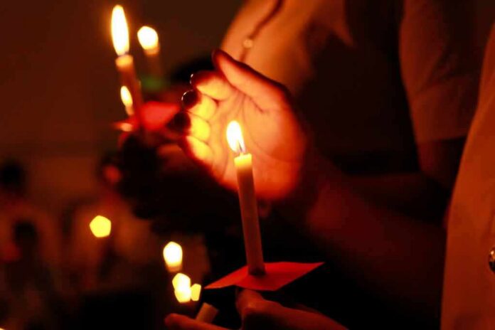 Hands holding lit candles in a dark setting