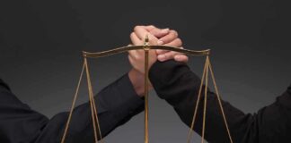 Gold balance scale with two hands arm wrestling behind it