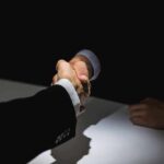 Two people in suits shaking hands over a table