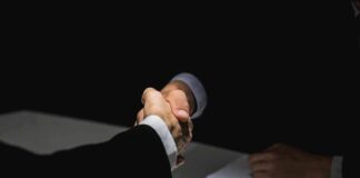 Two people in suits shaking hands over a table