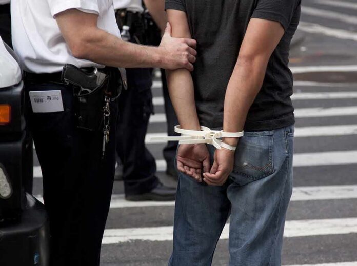 police officer detains person with hands zip-tied behind back