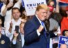 man in suit raising fists at a rally podium