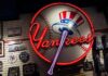 Who’s Really Running The Yankees? Neon Yankees sign on a wall of baseball memorabilia