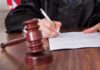 A judge signing a legal document with a gavel in the foreground