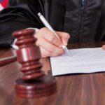 A judge signing a legal document with a gavel in the foreground