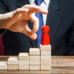 Businessperson hand above red figure on wooden block steps