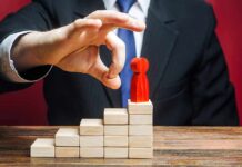 Businessperson hand above red figure on wooden block steps