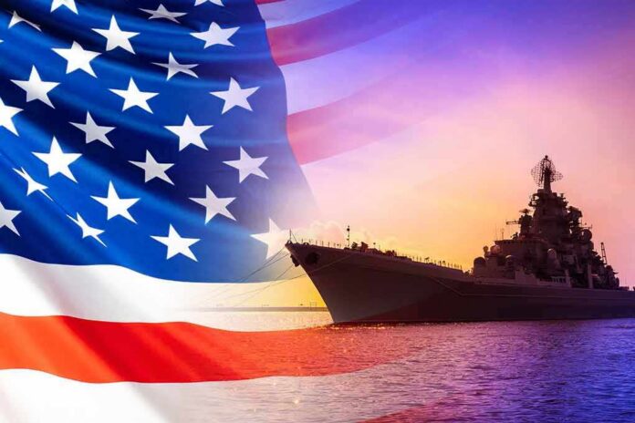 shutterstock_1709539462 United States flag overlay with a naval warship at sunset on the ocean