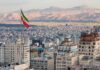 Iranian flag over a dense cityscape with mountains in the background