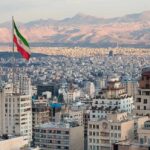 Iranian flag over a dense cityscape with mountains in the background