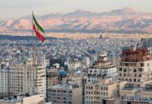 Iranian flag over a dense cityscape with mountains in the background