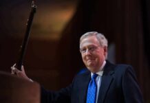 Health Blackout Engulfs McConnell — Why Hide? A man in a suit holding a gavel at a podium