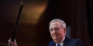 Health Blackout Engulfs McConnell — Why Hide? A man in a suit holding a gavel at a podium