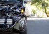 Front of a car with severe collision damage and exposed headlight