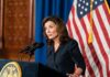Woman at podium speaking with microphones and U.S. flag behind