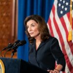 Woman at podium speaking with microphones and U.S. flag behind