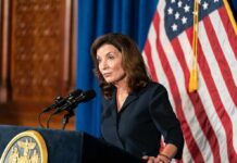 Hochul’s Anti-ICE Move CRUSHED Woman at podium speaking with microphones and U.S. flag behind