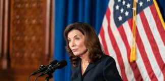 Hochul’s Anti-ICE Move CRUSHED Woman at podium speaking with microphones and U.S. flag behind