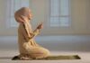 Woman in hijab praying on a mat indoors