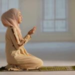 Woman in hijab praying on a mat indoors