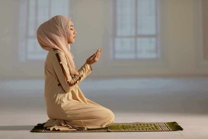 Woman in hijab praying on a mat indoors