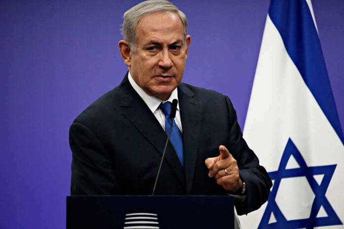 man in suit speaking at a podium with an Israeli flag