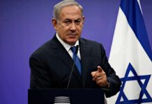 man in suit speaking at podium with Israeli flag