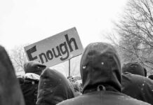 Justice Dept Targets ‘Hidden’ Transitions crowd in winter coats at a protest holding a sign