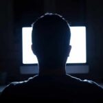 person silhouetted in front of a bright computer screen