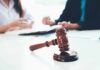 judge's gavel on table with people discussing documents in background